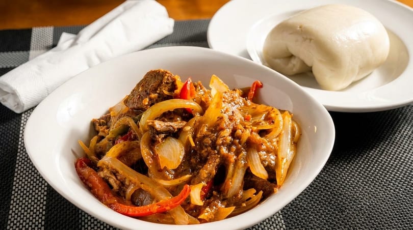 A bowl of spicy beef stir-fry with onions and peppers, served with a side of fufu.